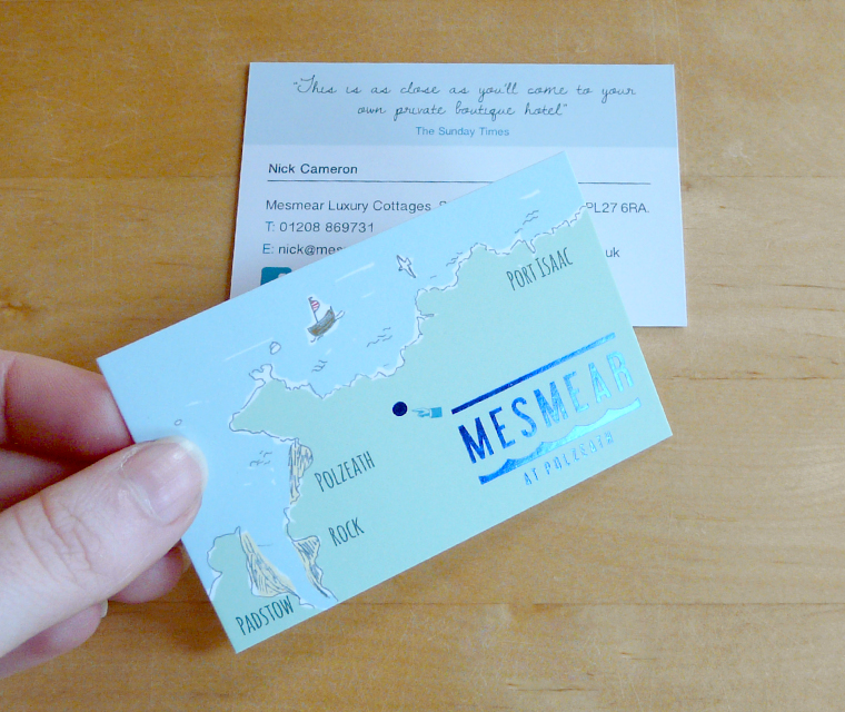 Mesmear business card held in hand showing the illustrated map and reflective blue foil logo