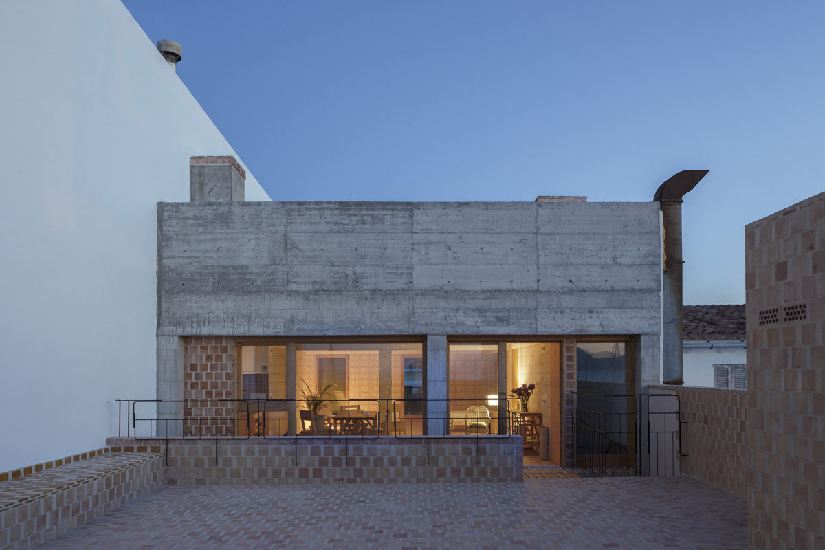 Modern home at night with a mixture of exposed concrete and terracotta tiles