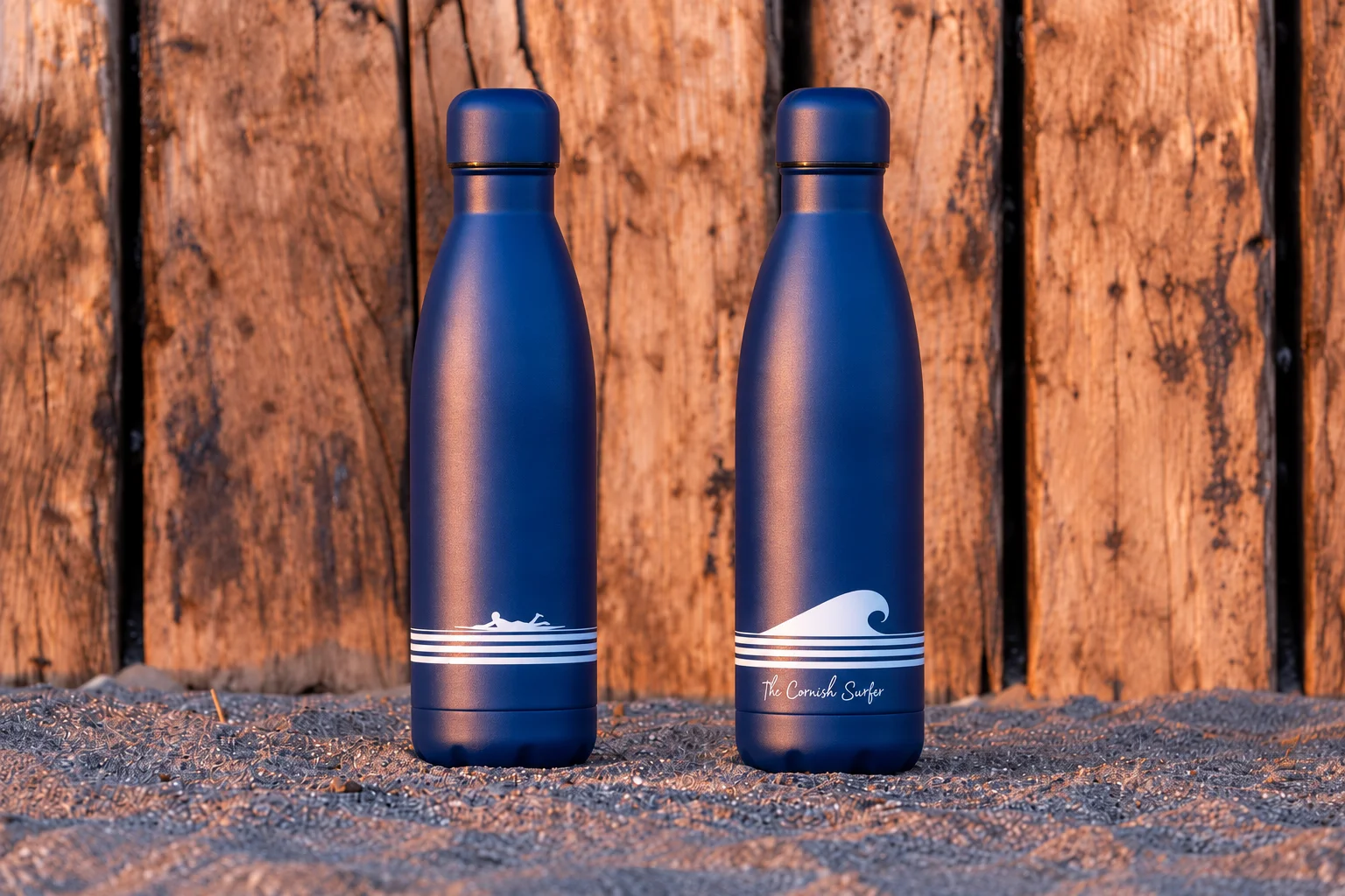 Two navy reusable bottles featuring The Cornish Surfer wave and surfer artwork