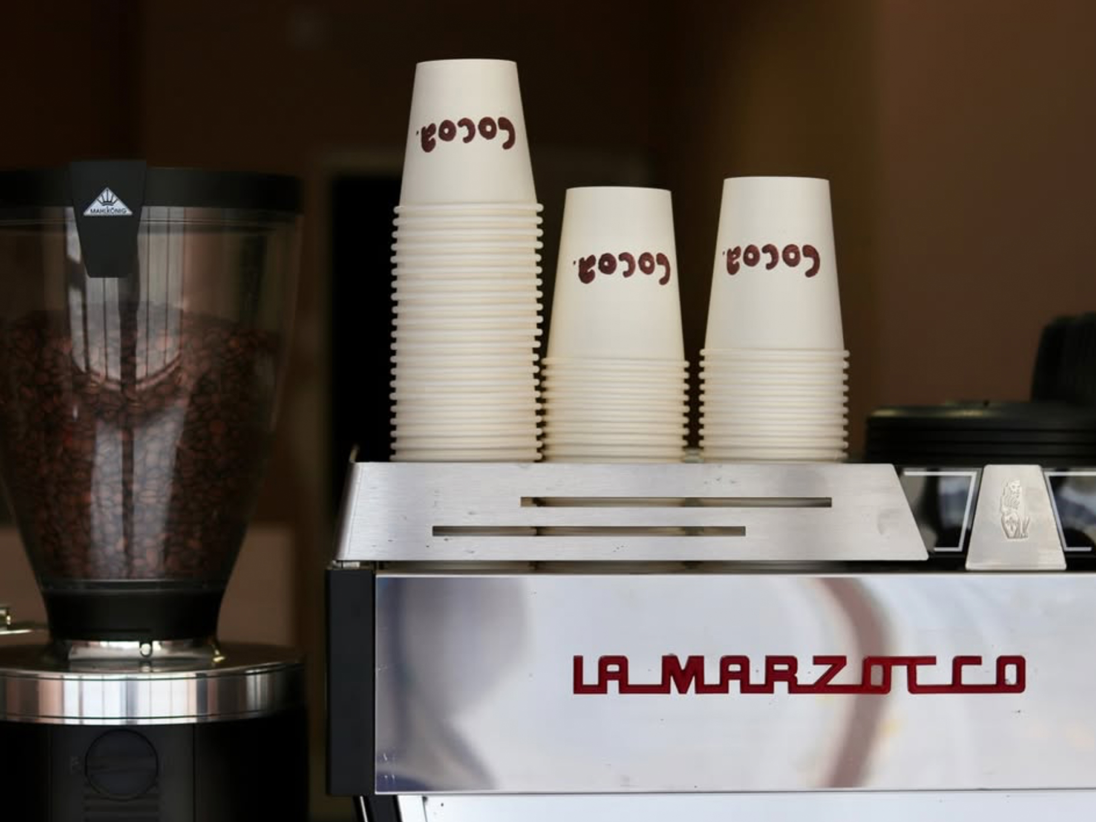 Cocoa branded coffee cups with stamped logo beside a coffee machine